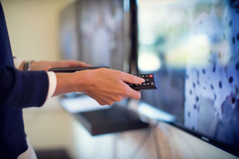 Kvinna håller fjärrkontroll till TV i handen.
