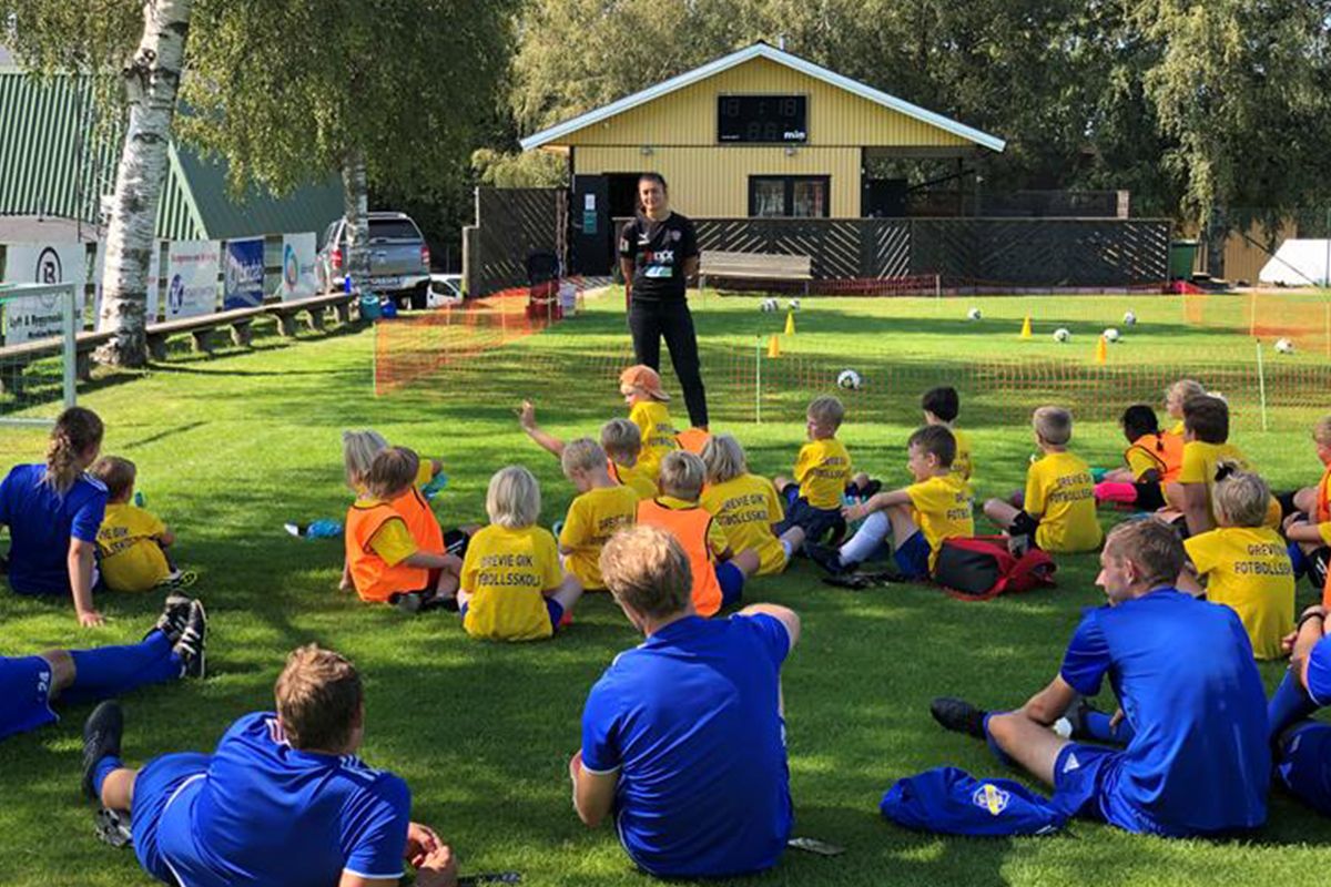 Barn sitter på gräset och lyssnar på tränare