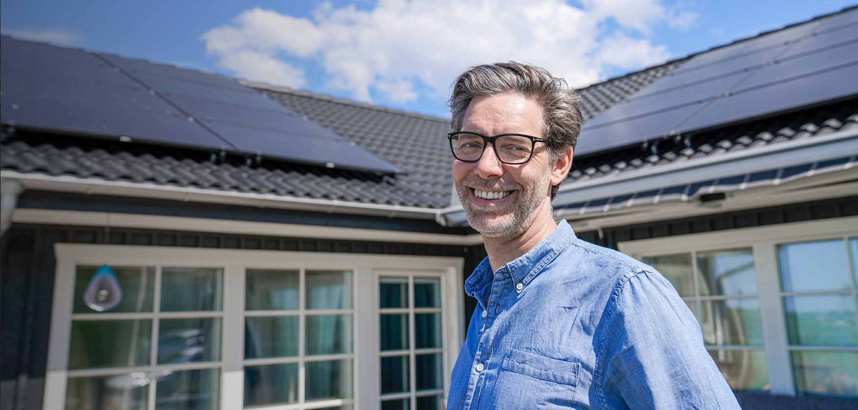 Glad man står framför villa med solceller från Bjäre Kraft och har gjort en bra investering.