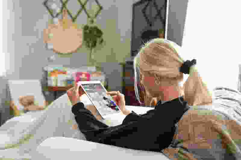Ung tjej under filt med iPad i fåtölj