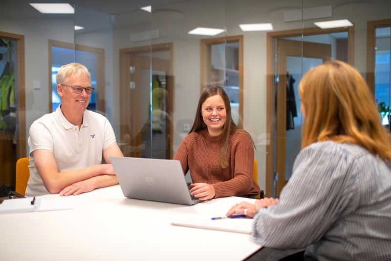Tre glada medarbetare sitter i ett kontor med glasväggar på Bjäre Kraft.
