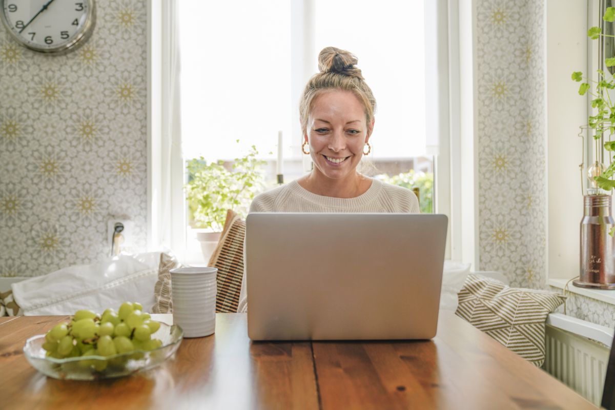 Kvinna jobbar på sin laptop hemma vid köksbordet