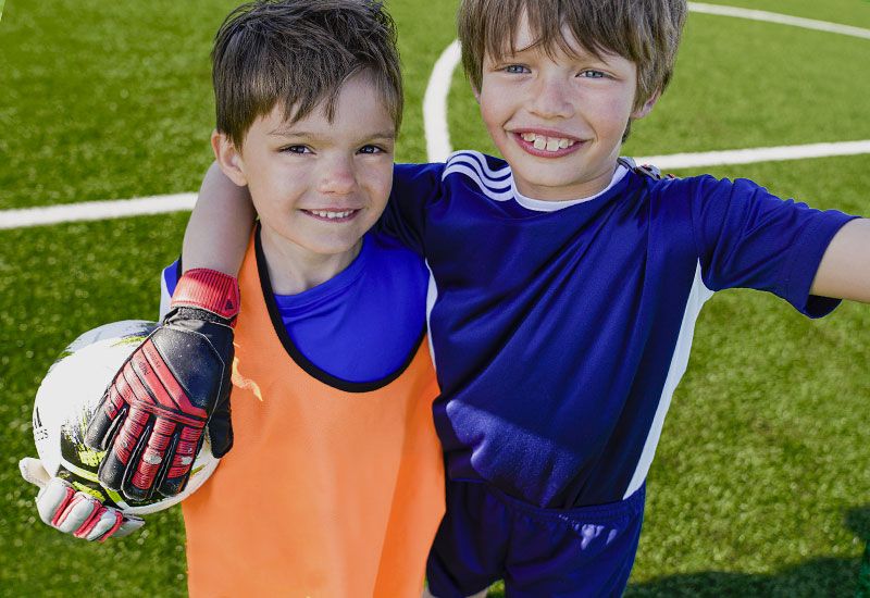 2 unga glada pojkar som håller i fotboll på en fotbollsplan