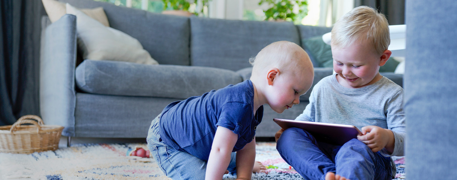 Två unga killar sitter och kollar på en iPad i ett vardagsrum